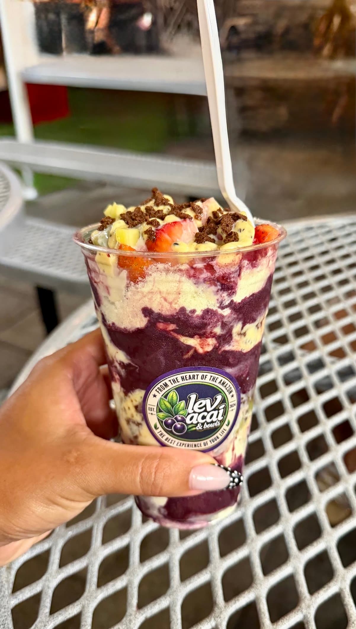 A hand holding a LEV açaí cup layered with fruit and granola